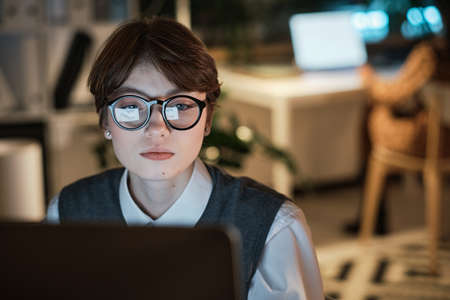 Young businesswoman in eyeglasses concentrating on her online work, she working on laptop at office till late eveningの写真素材