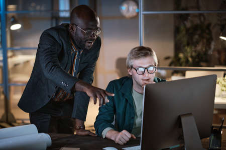 African businessman pointing at computer monitor and discussing online project with his colleague...