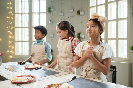 Group of children in aprons standing near the table with cutting board, they learning to cook at cooking lessonの写真素材