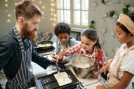 Group of children putting the dough on the waffle iron and learning to bake waffles with the help of chefの写真素材