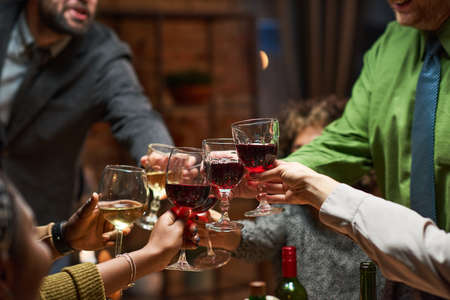 Close-up of group of people toasting glasses with red wine during a party at homeの写真素材