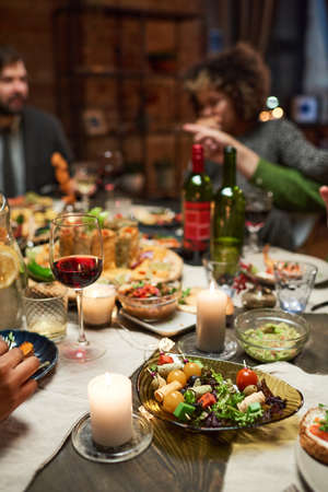 Close-up of dining table with delicious dishes and glasses of red wine with people sitting in the backgroundの写真素材