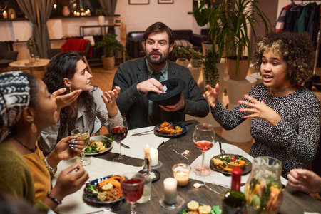 Group of friends sitting at dining table talking and playing games during a dinner party