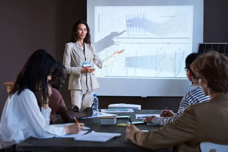 Group of business people sitting at the table and listening to the speaker who pointing at big monitor at conferenceの写真素材