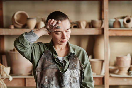 Female potter in apron looking very tired, she having a lot of work in pottery workshopの写真素材