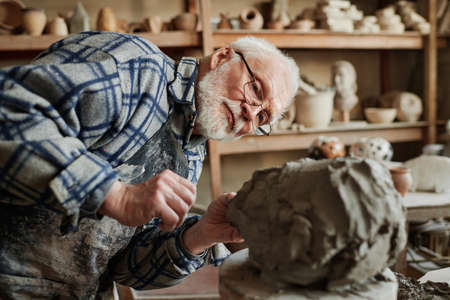 Senior man concentrating on his work in studio, he making ceramic sculpture on wheel