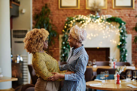 Two African women smiling and embracing each other during their meeting in the restaurantの写真素材