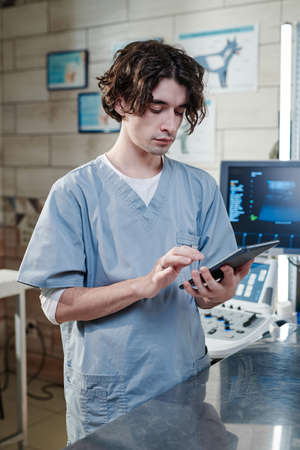 Serious doctor concentrating on his online work, he typing on digital tablet while standing at medical clinicの写真素材