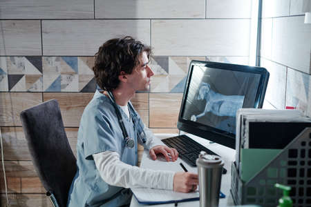 Young vet doctor sitting at the table in front of the computer monitor and examining the x-ray image...