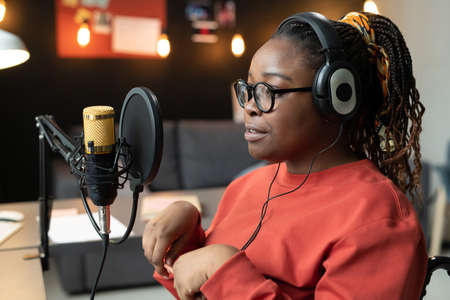 African young woman in headphones speaking to the microphone, she recording online talk in the room