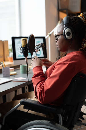 African woman sitting on wheelchair in front of the microphone and having a live stream in the roomの写真素材
