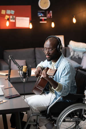 African man with disability playing guitar and singing song while recording his podcast at homeの写真素材