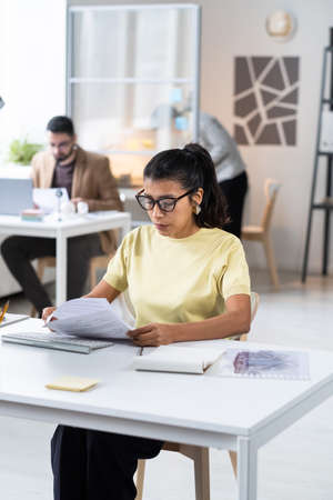 Serious businesswoman in eyeglasses doing paperwork at office, she sitting at her workplace and reading a contractの写真素材