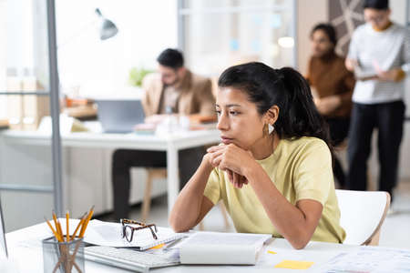 Serious businesswoman sitting at her workplace with documents with pensive expression, she working...