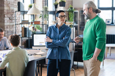 Businessman talking to businesswoman while they standing at board room during business meeting with colleaguesの写真素材