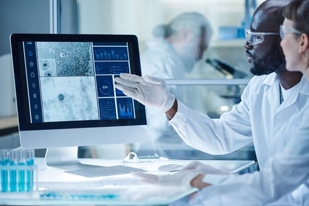 African male scientist pointing at computer monitor with micro image of bacterium and discussing it...