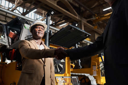 African businessman in suit shaking hands with partner and greeting him during meeting in factoryの写真素材
