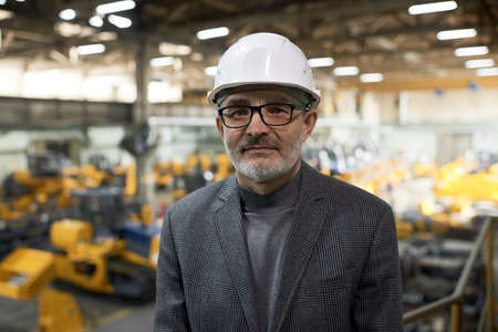 Portrait of elder engineer in hardhat looking at camera while running the process in plant