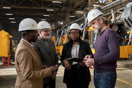Group of business people in work helmets discussing the supply of new equipment together standing in warehouseの写真素材