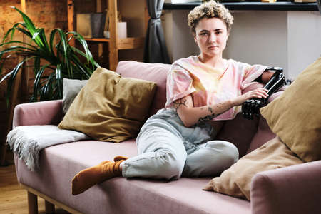 Portrait of young woman with prosthetic arm sitting on sofa in living room