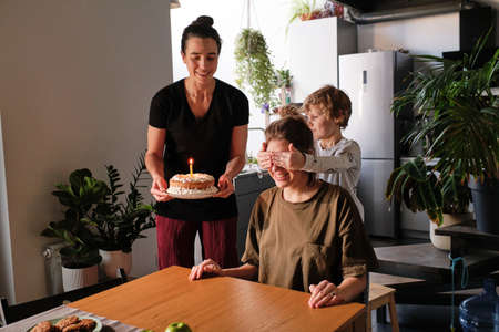 Lesbian family with little son celebrating birthday of mother with cake together in kitchenの写真素材