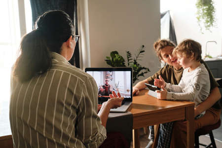 Rear view of businesswoman having online meeting on laptop sitting at table, she working at home...