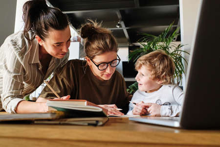 Young homosexual mothers teaching their little son together at table with booksの写真素材