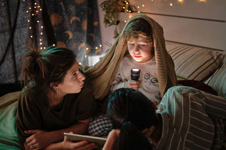 Little boy sitting under blanket with flashlight and telling scary tales to his homosexual mothers...