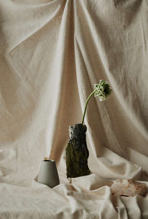 Vertical contemporary still life shot of flower branch, small ceramic vase and granite stone against linen fabric draperyの写真素材