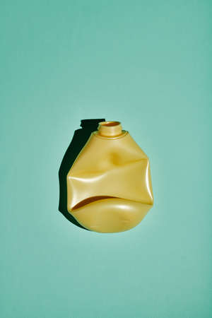 Vertical top-down shot of crumpled yellow plastic bottle on light blue background, conscious...