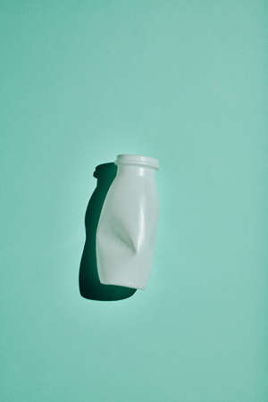 Vertical minimalistic flat lay shot of white plastic bottle on bluish green background, conscious consumption and recycling conceptの写真素材