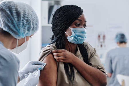 African young woman in mask protecting herself during pandemic, she getting vaccine from nurse at hospitalの写真素材