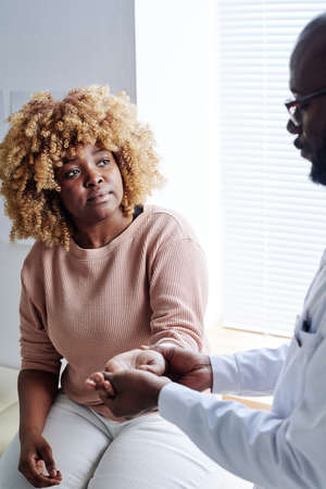 African woman with curly hair sitting at office while doctor examining herの写真素材