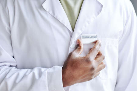 Close-up of African male doctor attaching badge on his white coatの写真素材