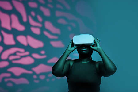 Black young woman in wireless goggles watching virtual reality against the pink pattern backgroundの写真素材