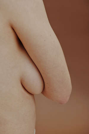 Side view of young woman hiding her breast with hand and showing her perfect body isolated on brown backgroundの写真素材