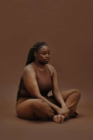 Portrait of young black woman in casual clothing sitting with blank expression isolated on brown backgroundの写真素材