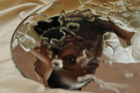 Close-up of reflection of young African woman looking through drops in mirror