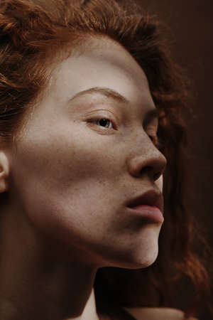 Close-up of young woman with red hair and freckles on her face having natural beauty