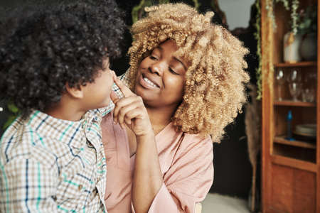 African smiling mother with curly hair playing with her son while he sitting on her knees