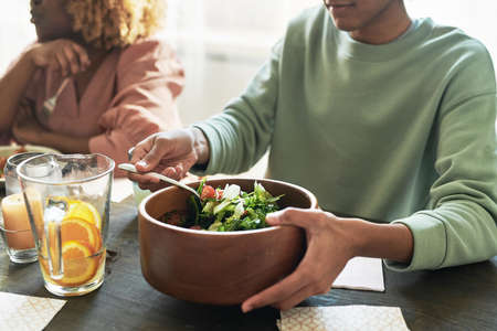 Close-up of teenage boy sitting at table and eating vegetable salad during dinner with his familyの写真素材