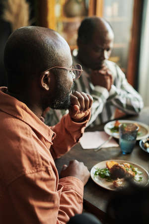 African man in eyeglasses sitting at table and having dinner with his family at homeの写真素材