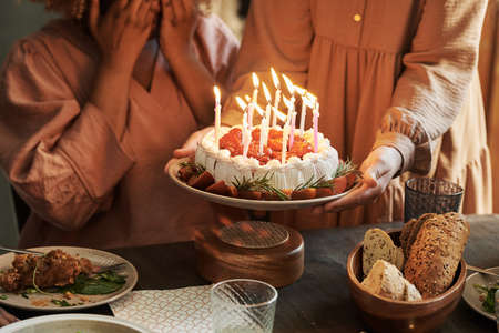 Close-up of family celebrating birthday with birthday cake with candles at dining tableの写真素材