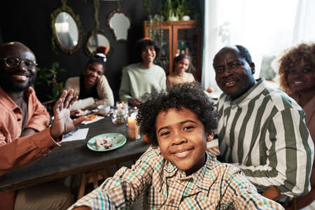 Cute little boy making selfie portrait of his big family while they sitting at table with cake and teaの写真素材