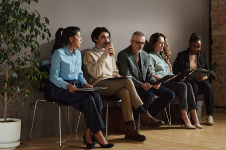 Group of people sitting on chairs in waiting room with resumes and waiting for their turn to job...
