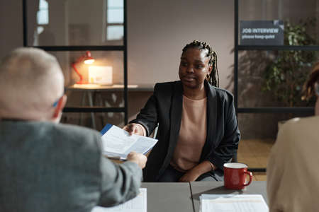 African young woman giving her resume to employer during her competition to get a new jobの写真素材