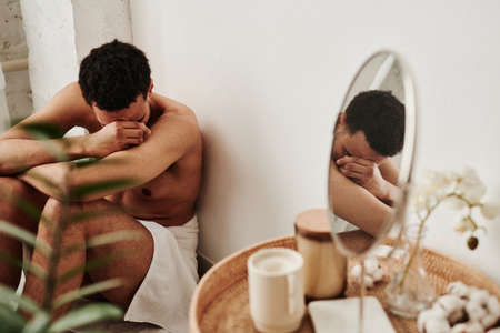 Young man covering his face with hands and crying on floor in bathroom, he having emotional stressの写真素材