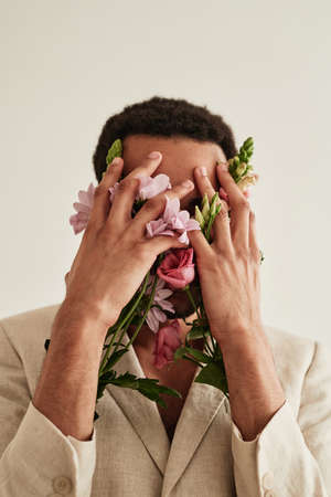 Portrait of young man covering his face with hands with flowers against the white backgroundの写真素材