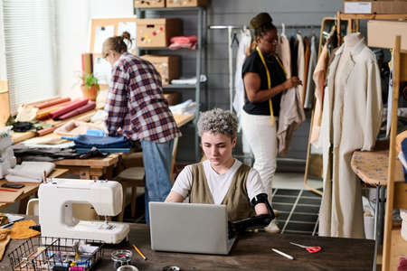 Group of young intercultural female tailors working over new fashion collection with girl having...