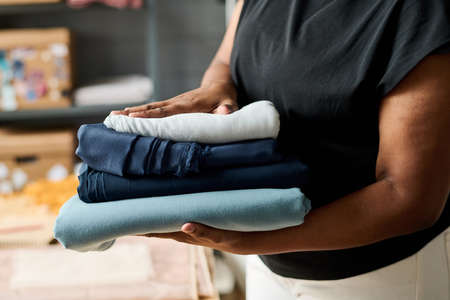 Close-up of young African American female tailor carrying stack of folded textile prepared for new seasonal collection of trendy apparelの写真素材